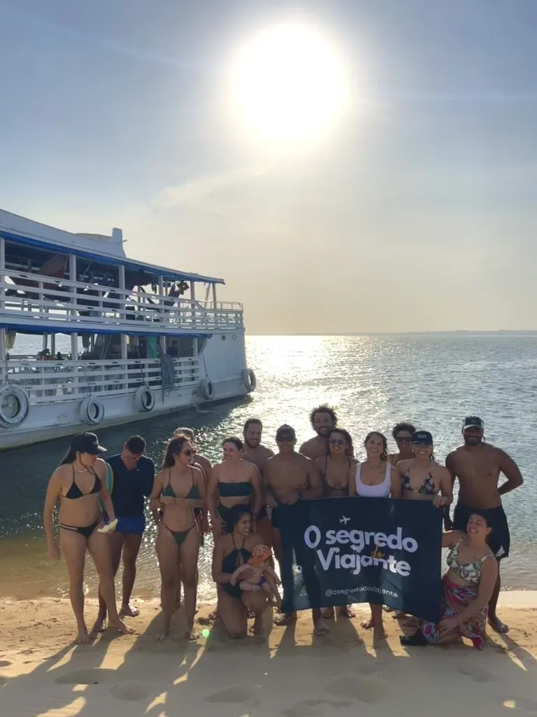Grupo da comunidade OSV com a bandeira O Segredo do Viajante na praia de Alter do Chão, ao pôr do sol
