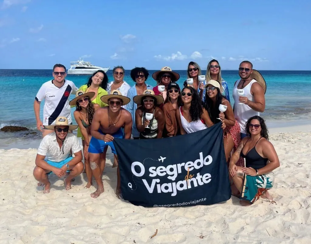 Grupo da comunidade OSV na praia em Curaçao com a bandeira O Segredo do Viajante